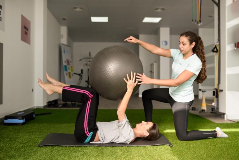 Clinical-pilates-physical-therapist-assisting-young-caucasian-woman-with-exercise